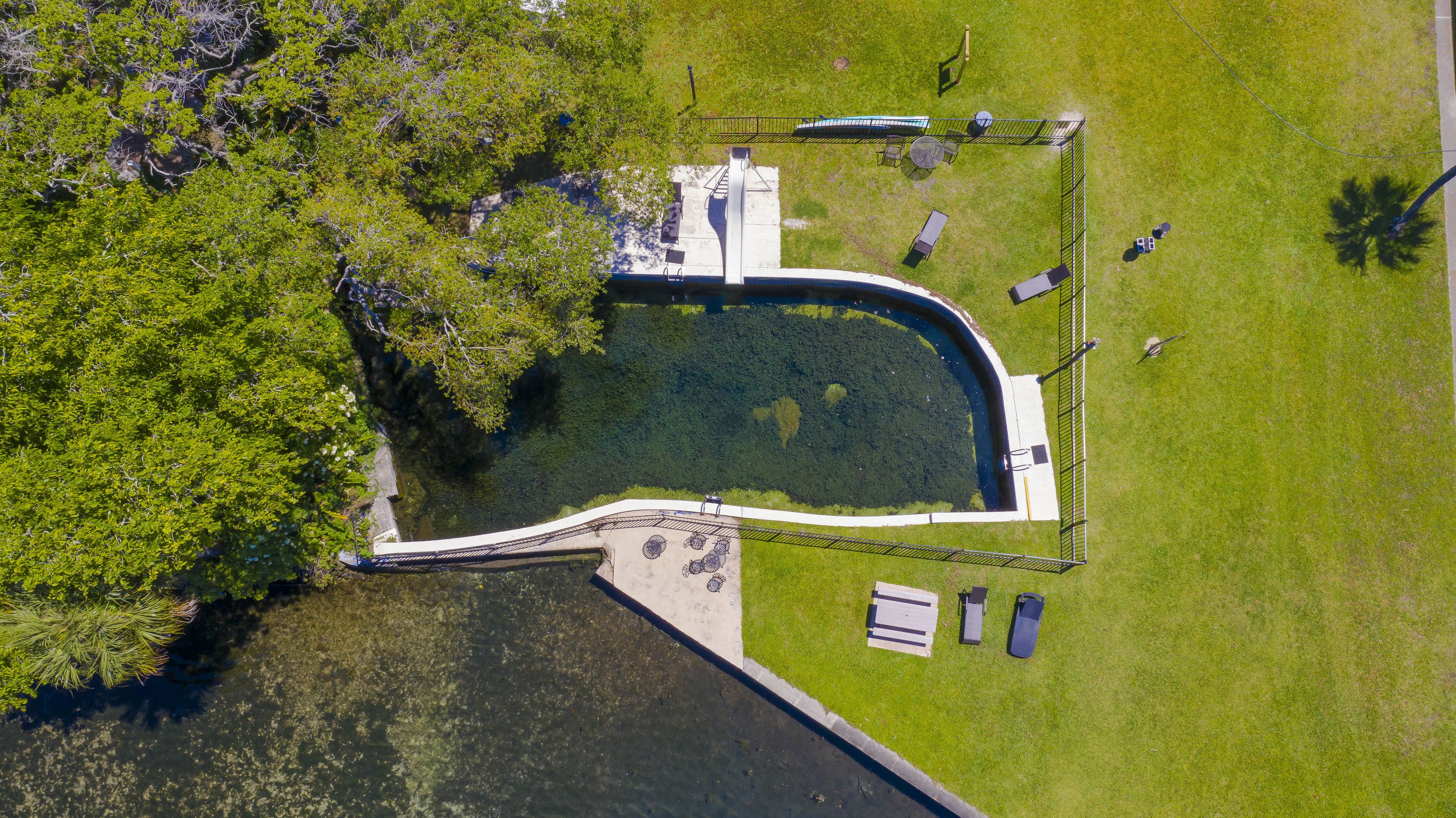 An aerial view of a park with a pond, a bridge, and a picnic area.