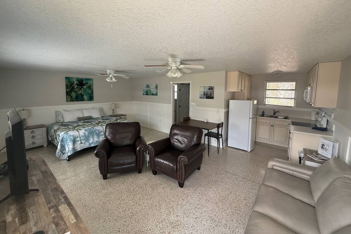 A compact living space with a bed, two leather chairs, a kitchenette, and a dining area.