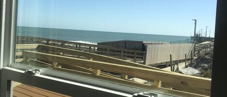 A view from a window overlooking a beach with a wooden bench and a fence.
