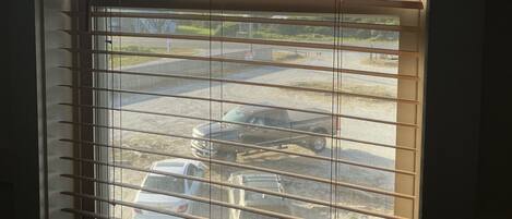 Una ventana con persianas horizontales, vista de coches aparcados afuera y un edificio visible en el fondo.