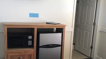 Habitación de hotel compacta con refrigerador y microondas integrados, un televisor de pantalla plana montado en la pared y una puerta que da a un pasillo.