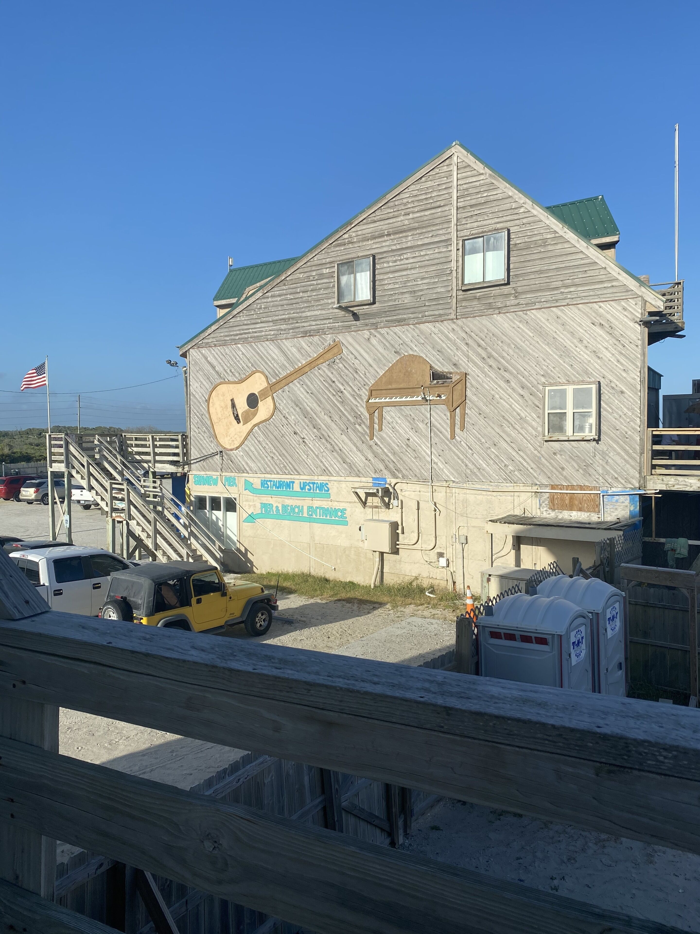 A building with a wooden facade, a guitar graphic, and signs for 'Restaurant Upstairs' and 'Pier & Beach Entrance'.