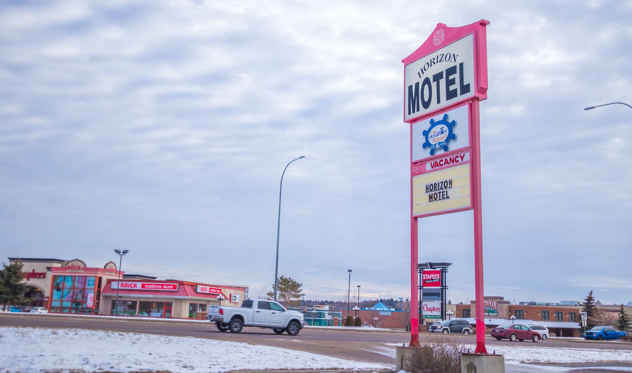 A motel sign with a 'Vacancy' label, a nearby 'The Atlantic Kitchen' restaurant, and a 'Staples' business depot.
