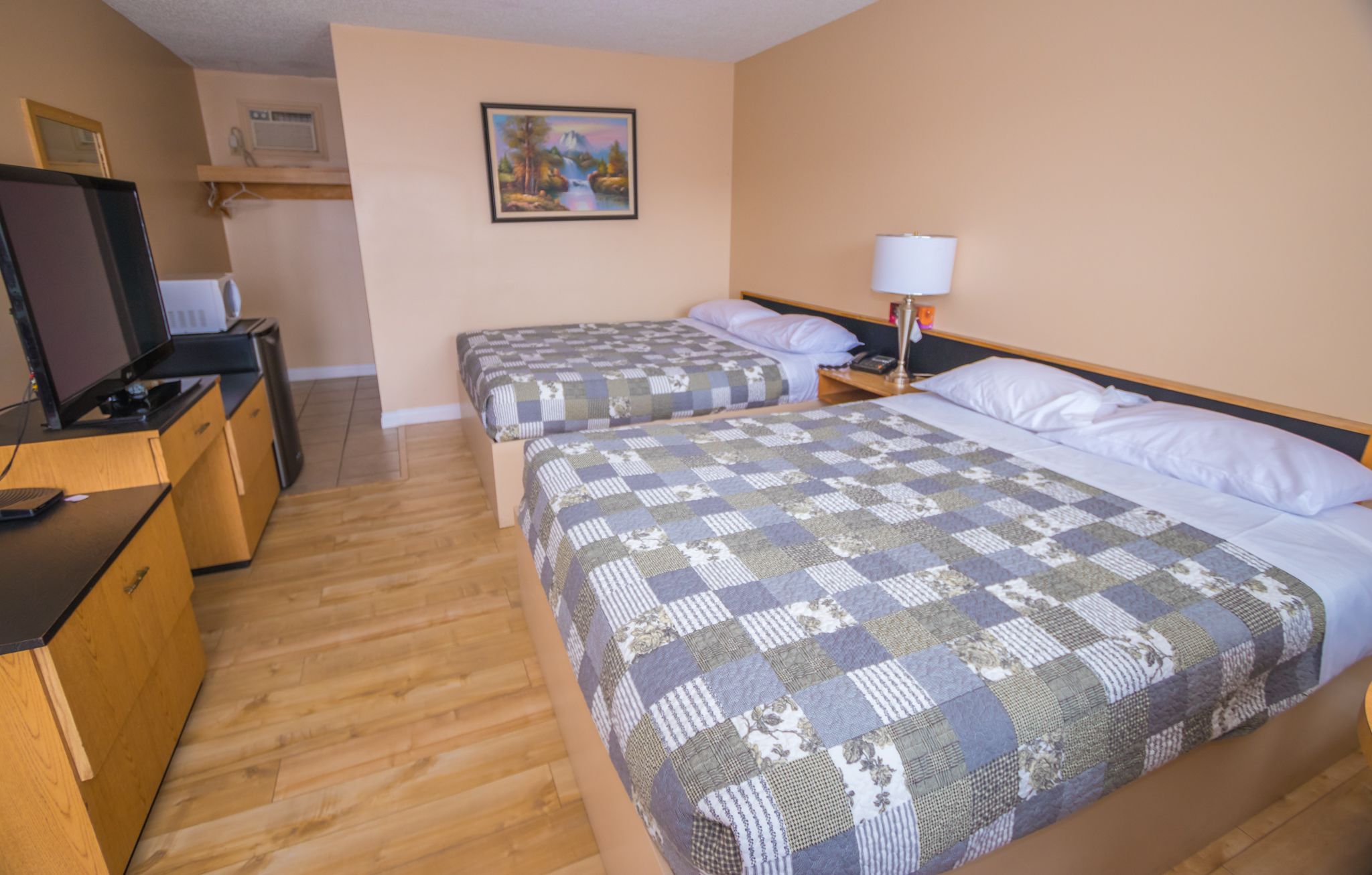A hotel room with two beds, a desk with a computer, a TV, and a painting on the wall.