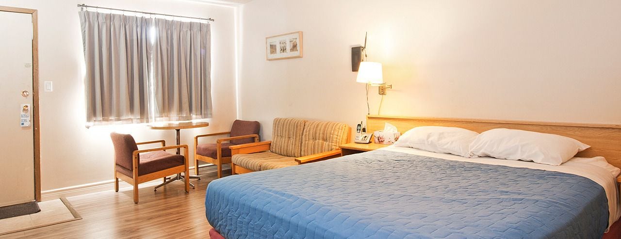 A hotel room with a bed, a sofa, two chairs, a table, a lamp, and a window with curtains.