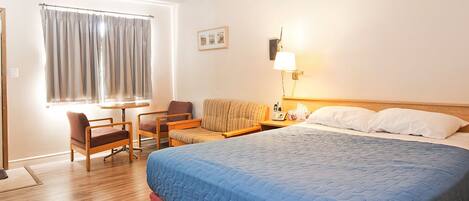 A hotel room with a bed, a sofa, two chairs, a table, a lamp, and a window with curtains.