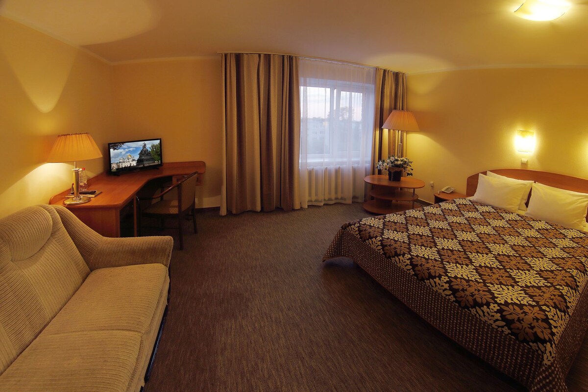 A hotel room with a bed, a desk, a chair, a TV, and a window with curtains.