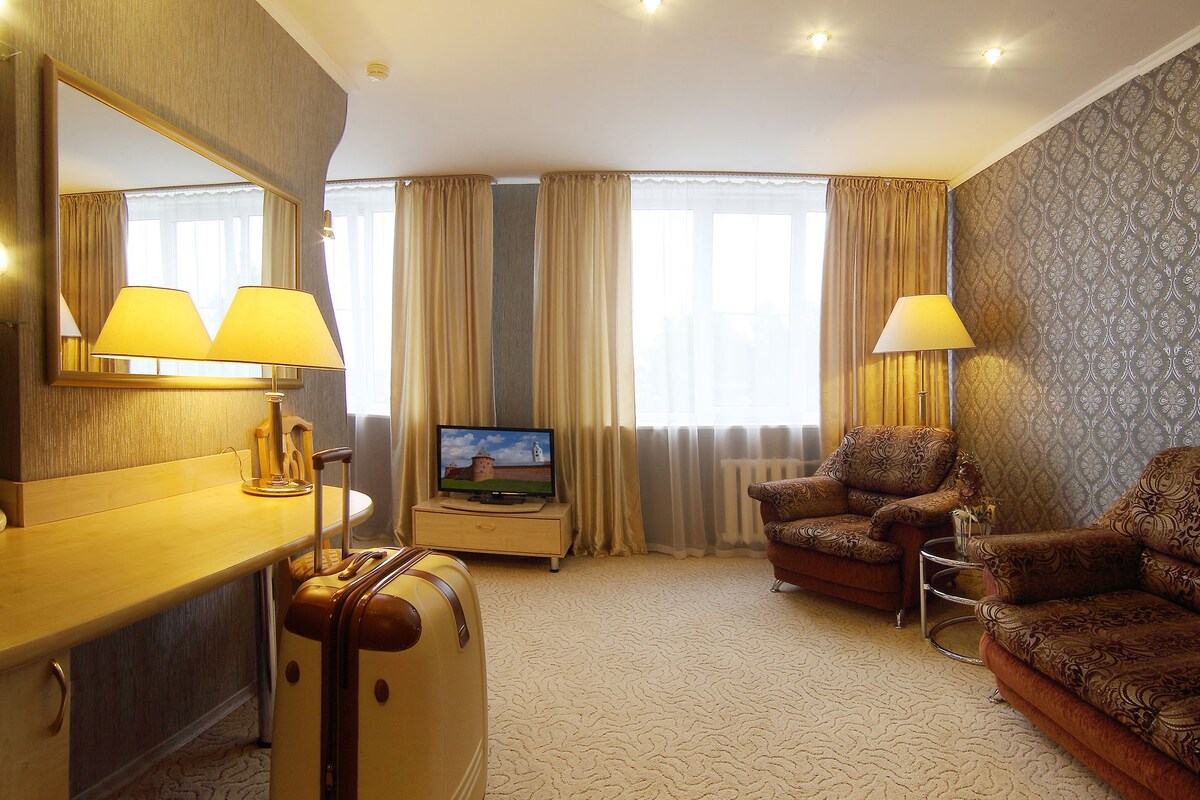 A hotel room with a wooden desk, a chair, a sofa, a television, and a large mirror.