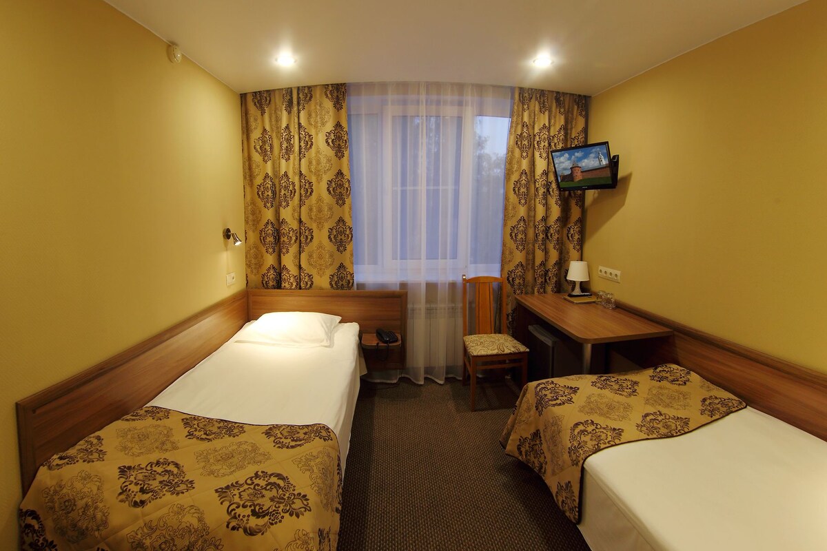A hotel room with two beds, a desk, a chair, a television, and a window with curtains.
