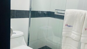 A modern bathroom with a white toilet, a glass shower enclosure, and a black tiled floor. - Hotel Baja del Sol Inn (Playas de Rosarito)