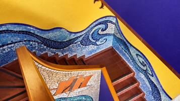 Una escalera con diseño de mosaico, barandilla de madera y un adorno de sol en la pared.