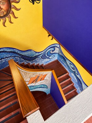 Un escalier orné d’une mosaïque, doté d’une rampe en bois et d’une décoration solaire sur le mur.