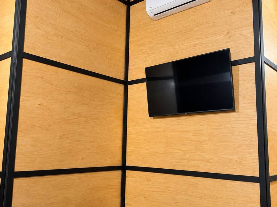 A room with a wooden panel wall, a mounted air conditioner, a flat-screen TV, and a black chair.