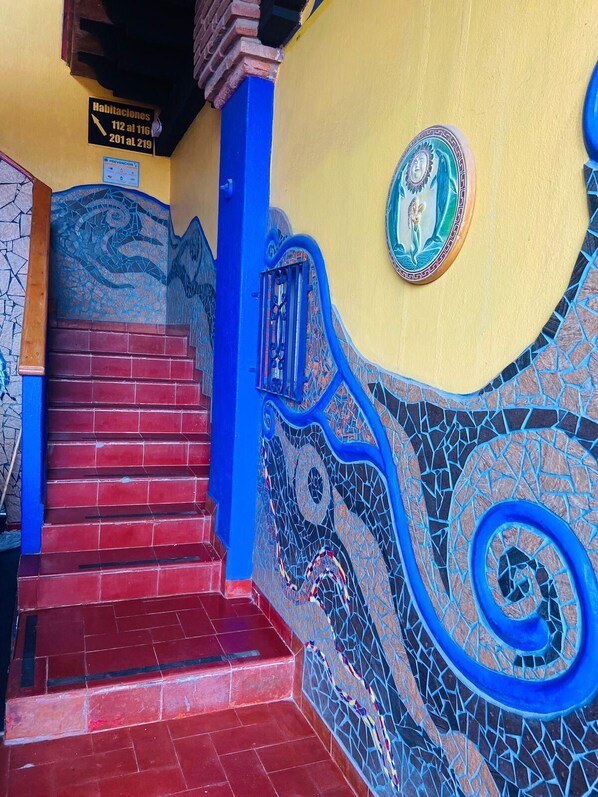 A staircase with red steps and blue accents, leading to a room with a mosaic wall and a decorative plate.