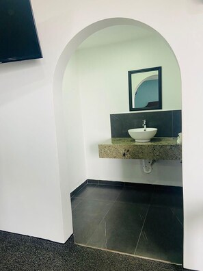 A bathroom with a white sink, a mirror, and a TV mounted on the wall.