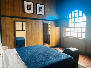 A bedroom with a large bed, a wardrobe, a mirror, and a window with a view.