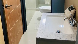 A modern bathroom with a wooden door, a white sink with a mirror, and a glass shower enclosure. - Hotel Baja del Sol Inn (Playas de Rosarito)