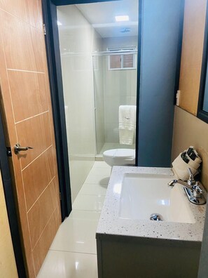 A modern bathroom with a wooden door, a white sink with a mirror, and a glass shower enclosure. - Hotel Baja del Sol Inn (Playas de Rosarito)