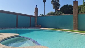 A swimming pool with a clear blue water, surrounded by a green wall and palm trees. - Hotel Baja del Sol Inn (Playas de Rosarito)
