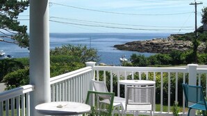 A balcony with white railings, a round table, and two chairs, overlooking a rocky coastline and the sea. - The Seafarer Inn (Rockport)