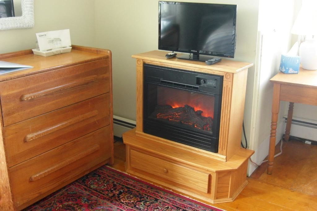 A room with a wooden dresser, a television on a wooden stand, and a fireplace with visible flames.