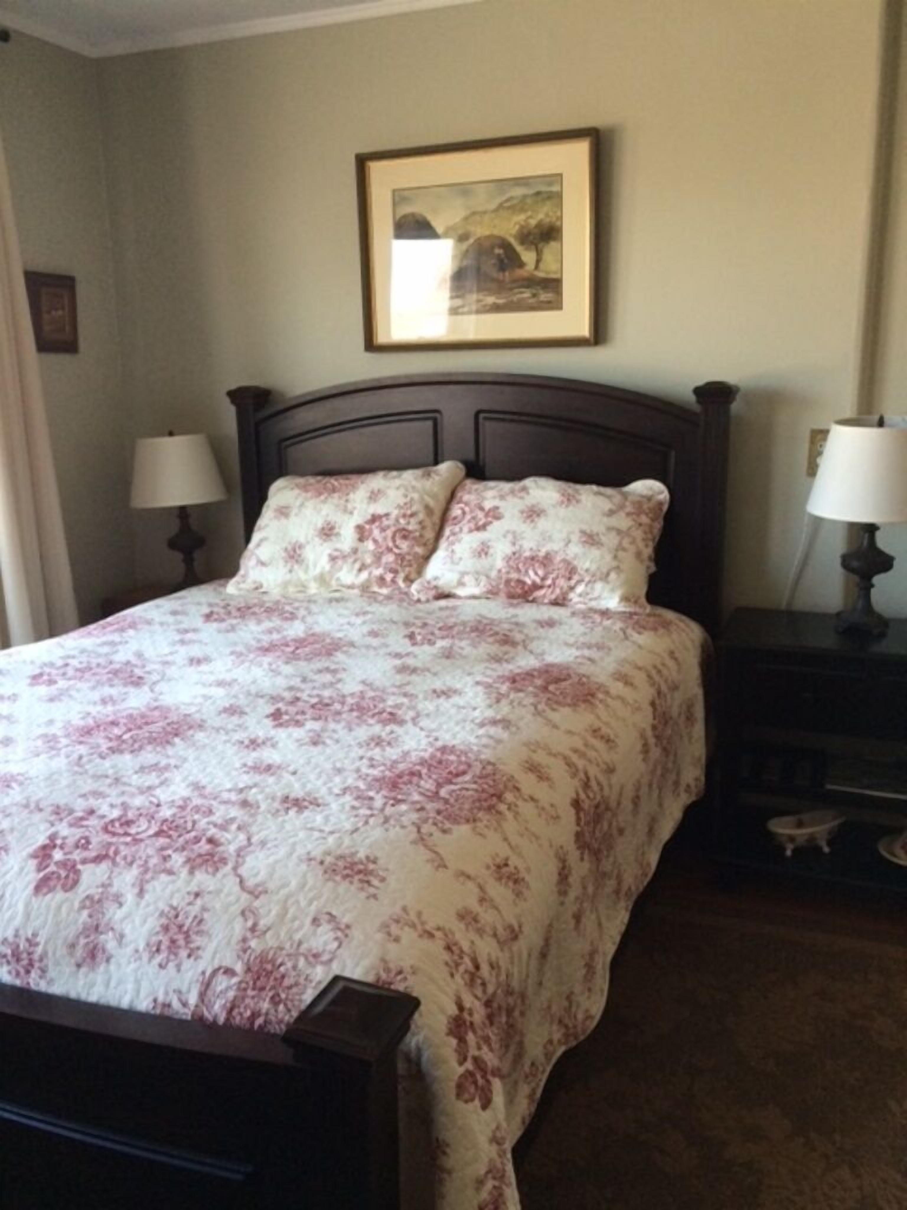 Una cama bien hecha con ropa de cama floral, dos lámparas de noche y un cuadro en la pared.