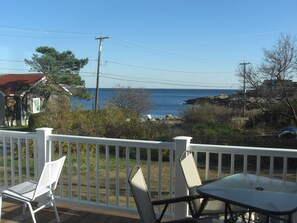 A deck with a white railing, two chairs, and a table overlooking a coastal view.
