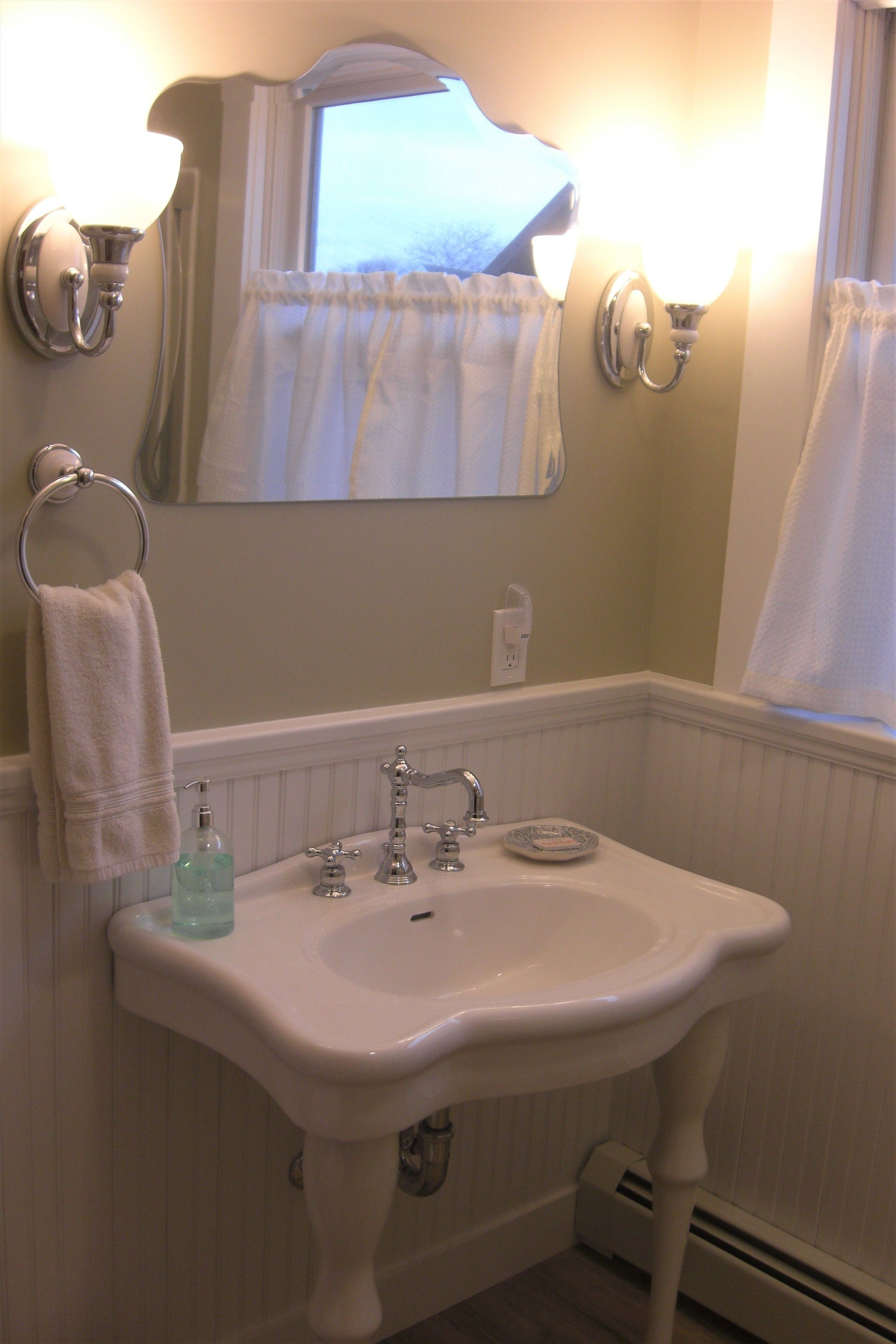 Un baño con un lavabo blanco, dos luces empotradas, un espejo y una ventana con cortinas.
