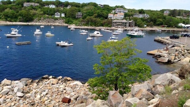 A marina with boats docked, surrounded by rocky terrain and residential buildings in the background. - The Seafarer Inn (Rockport)