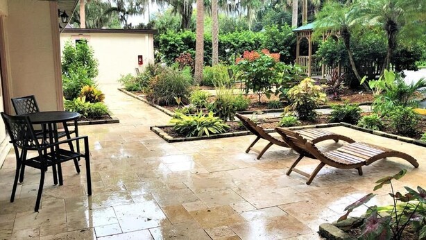 Un patio con mesa y sillas, rodeado de abundante vegetación y un pequeño elemento acuático.