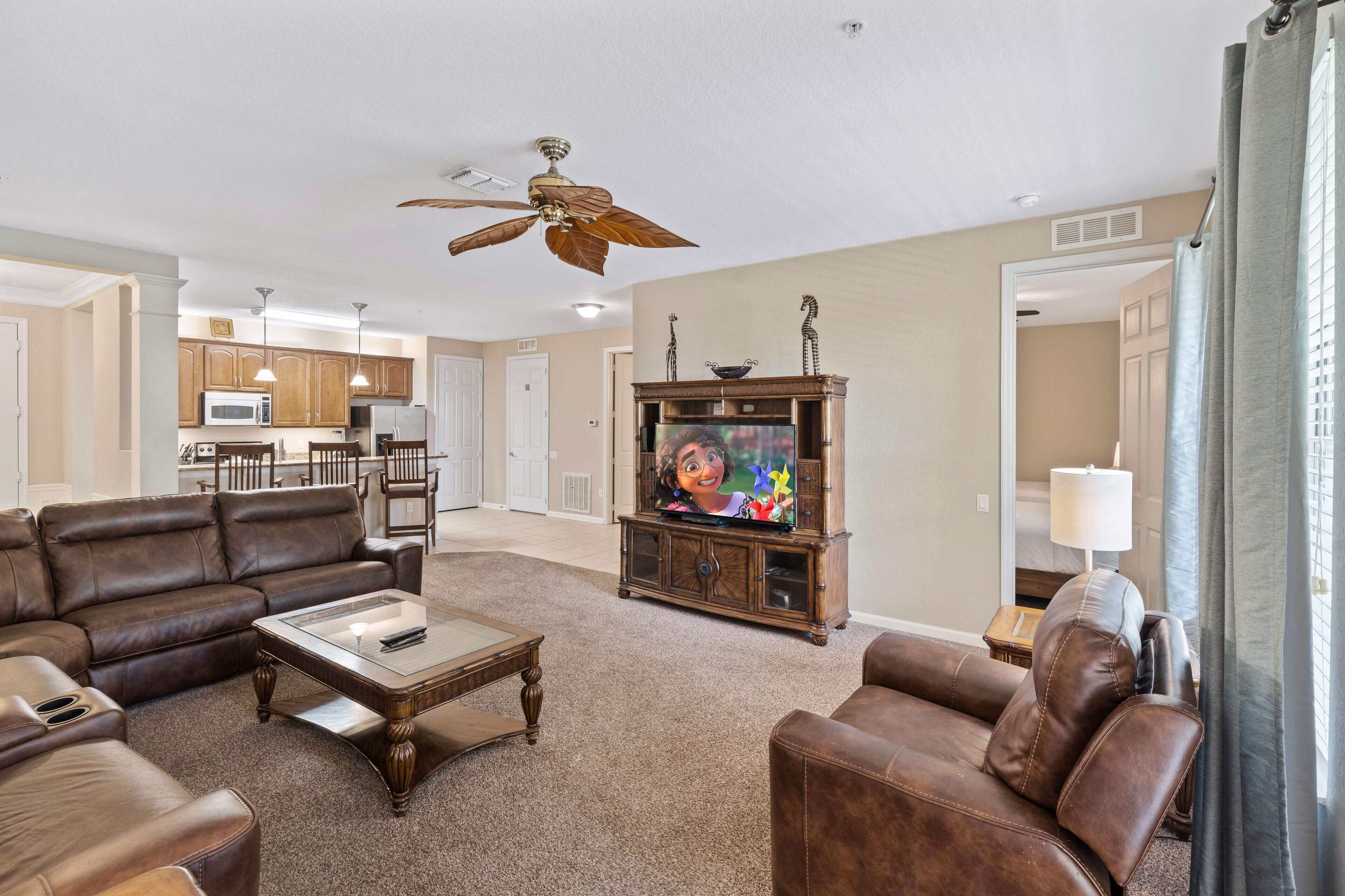 A spacious living room with a brown leather sofa, a glass coffee table, and a wooden entertainment center with a television.