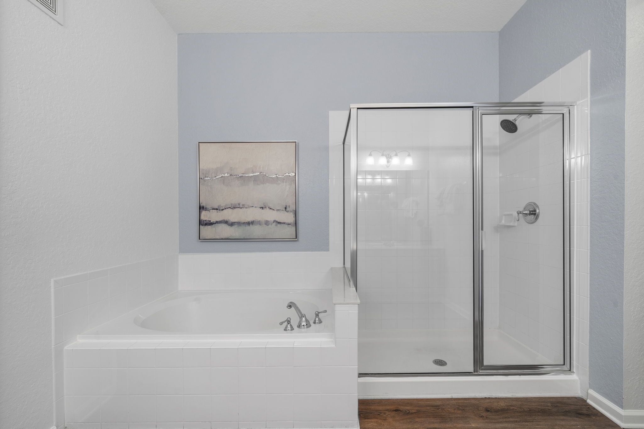 A bathroom with a glass-enclosed shower, a bathtub, and a wall-mounted artwork.