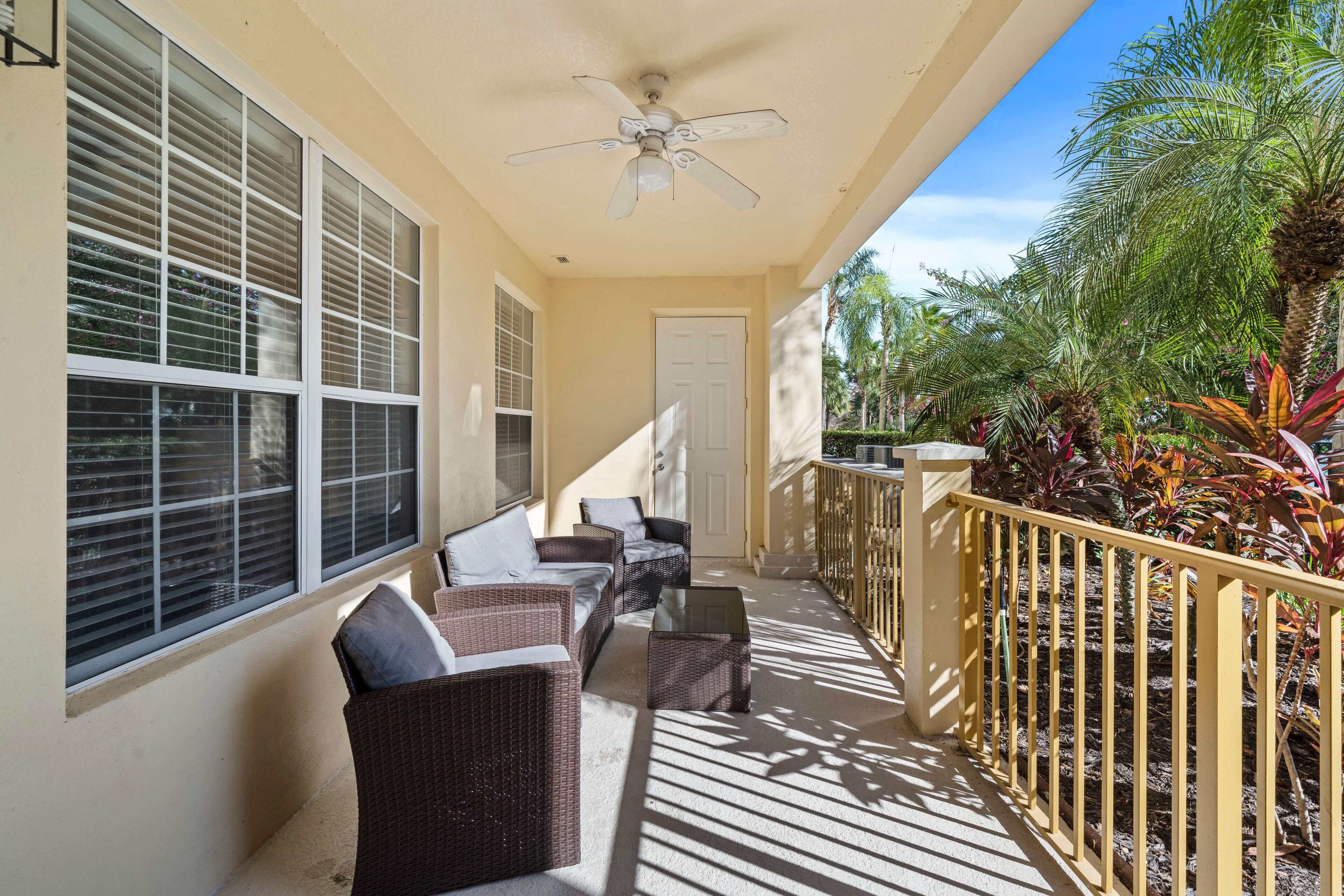 A covered outdoor area with wicker furniture, a ceiling fan, and a railing with plants.