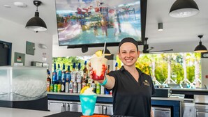 Een bar met een groot televisiescherm, een drankdispenser en een grill met groenten.