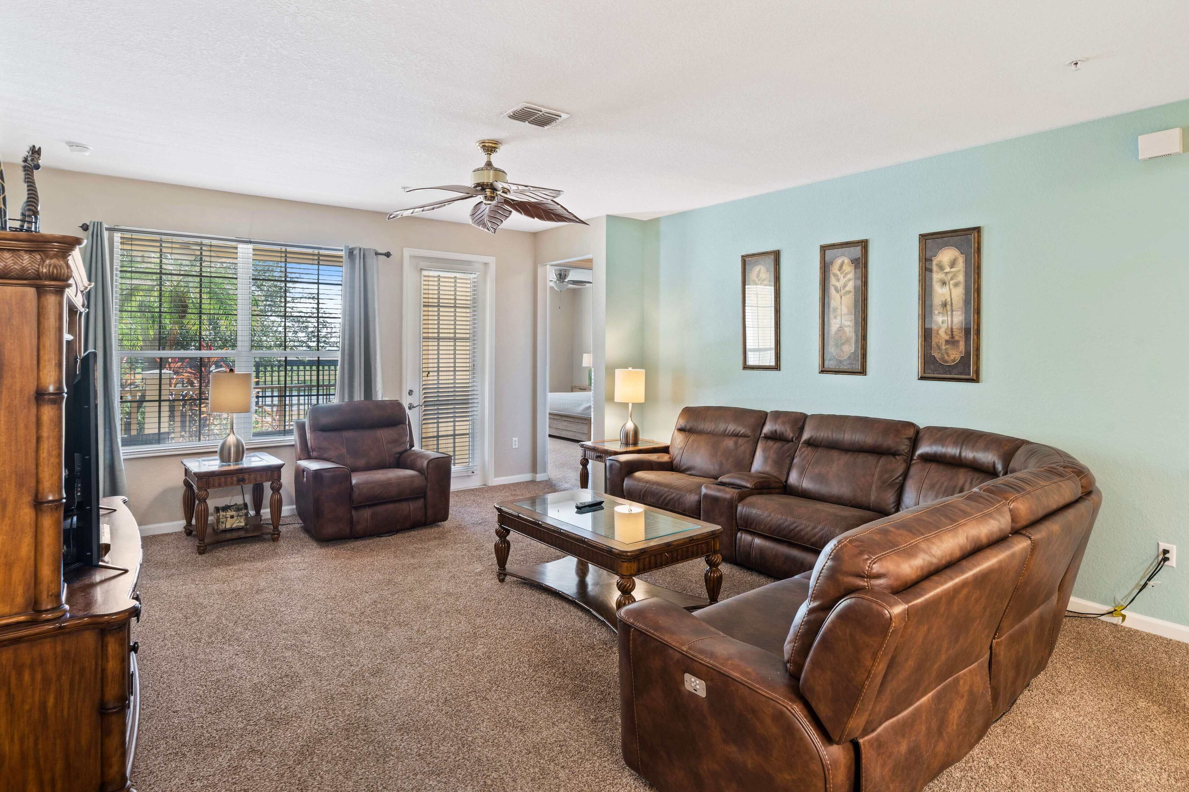 A living room with a brown leather sofa, a glass coffee table, and a ceiling fan.
