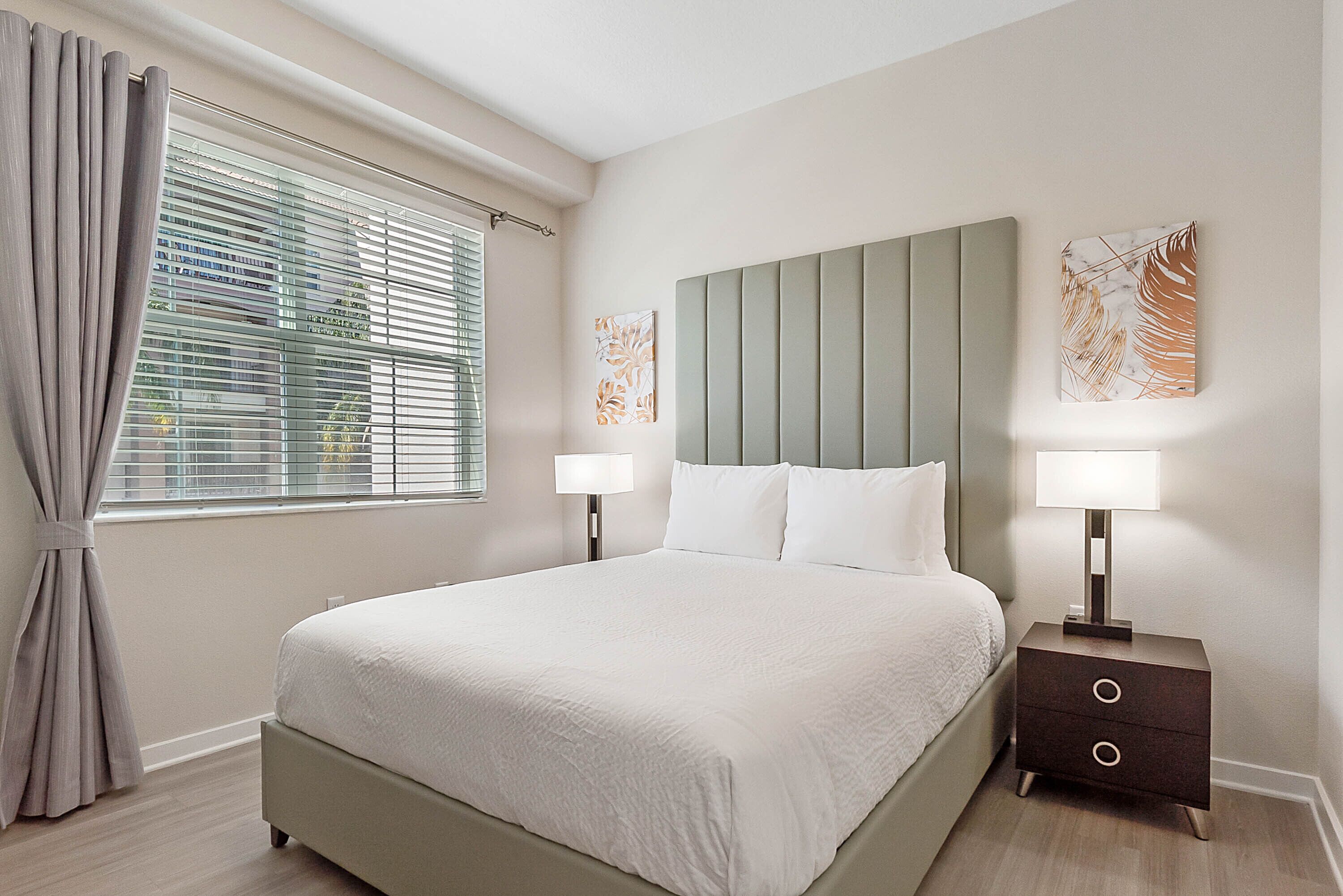 Une chambre à coucher bien aménagée, avec un grand lit, deux tables de chevet dotées de lampes et des œuvres d’art accrochées aux murs.