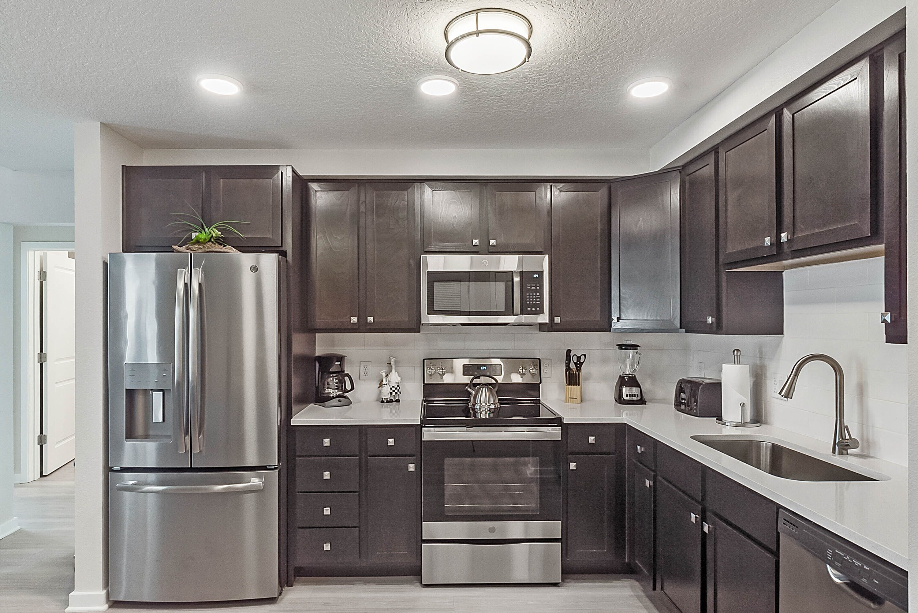 A modern kitchen with stainless steel appliances, dark cabinetry, and a white countertop.