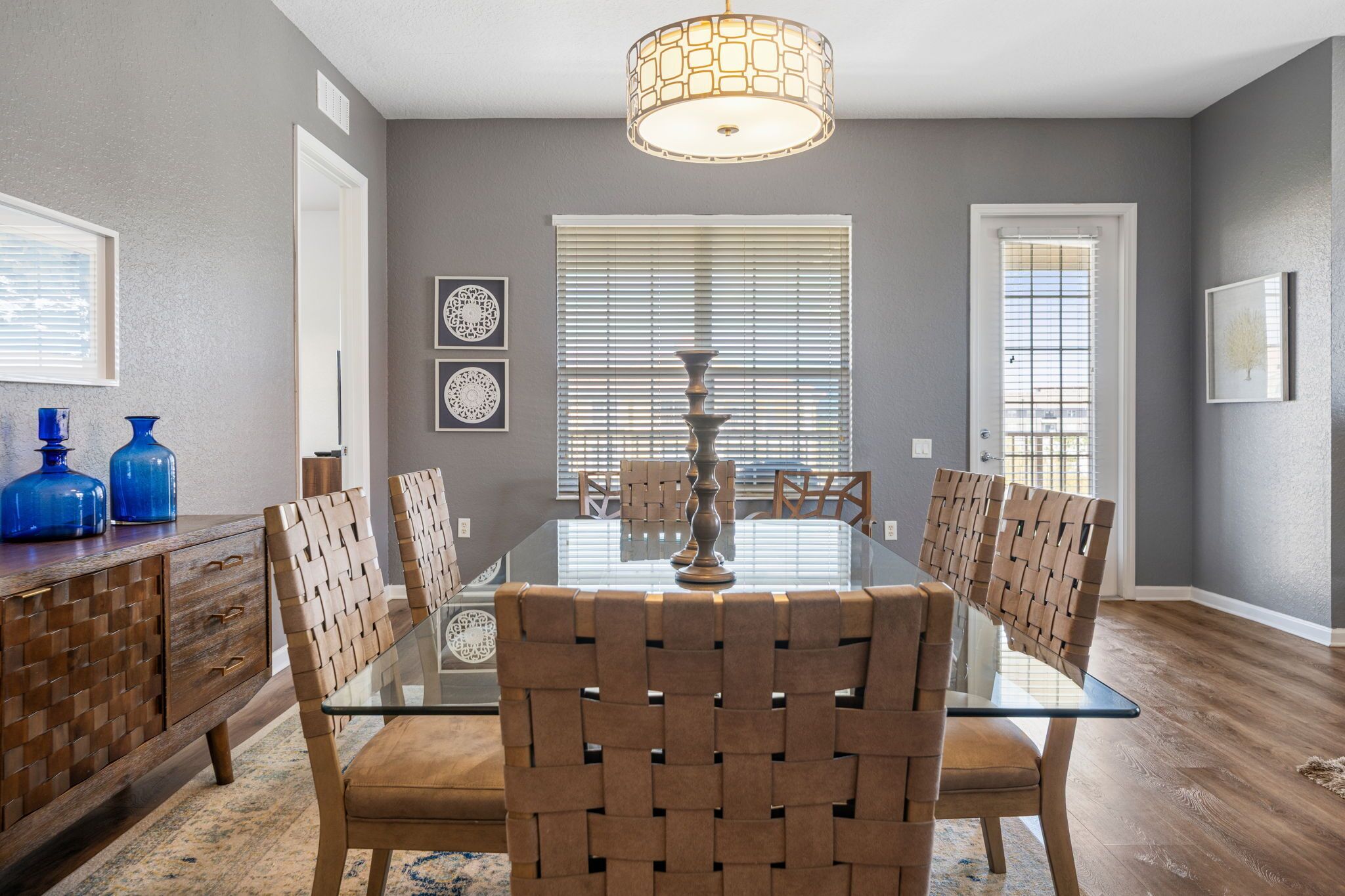 A dining room with a glass table, woven chairs, and a decorative vase.