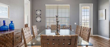 A dining room with a glass table, woven chairs, and a decorative vase.