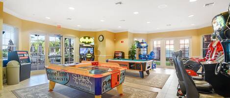 A brightly lit indoor recreational area with multiple foosball tables, arcade games, and a pool table.