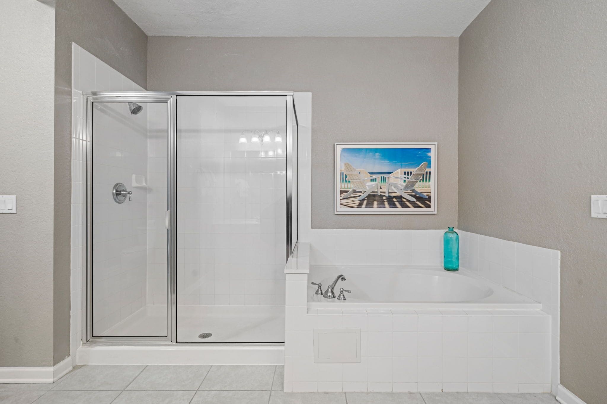 Un baño con ducha separada por mampara de vidrio, una bañera blanca y un cuadro enmarcado en la pared.