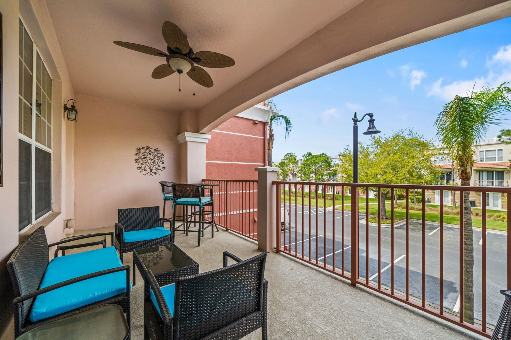 A balcony with wicker furniture, a ceiling fan, and a view of a parking lot and buildings.