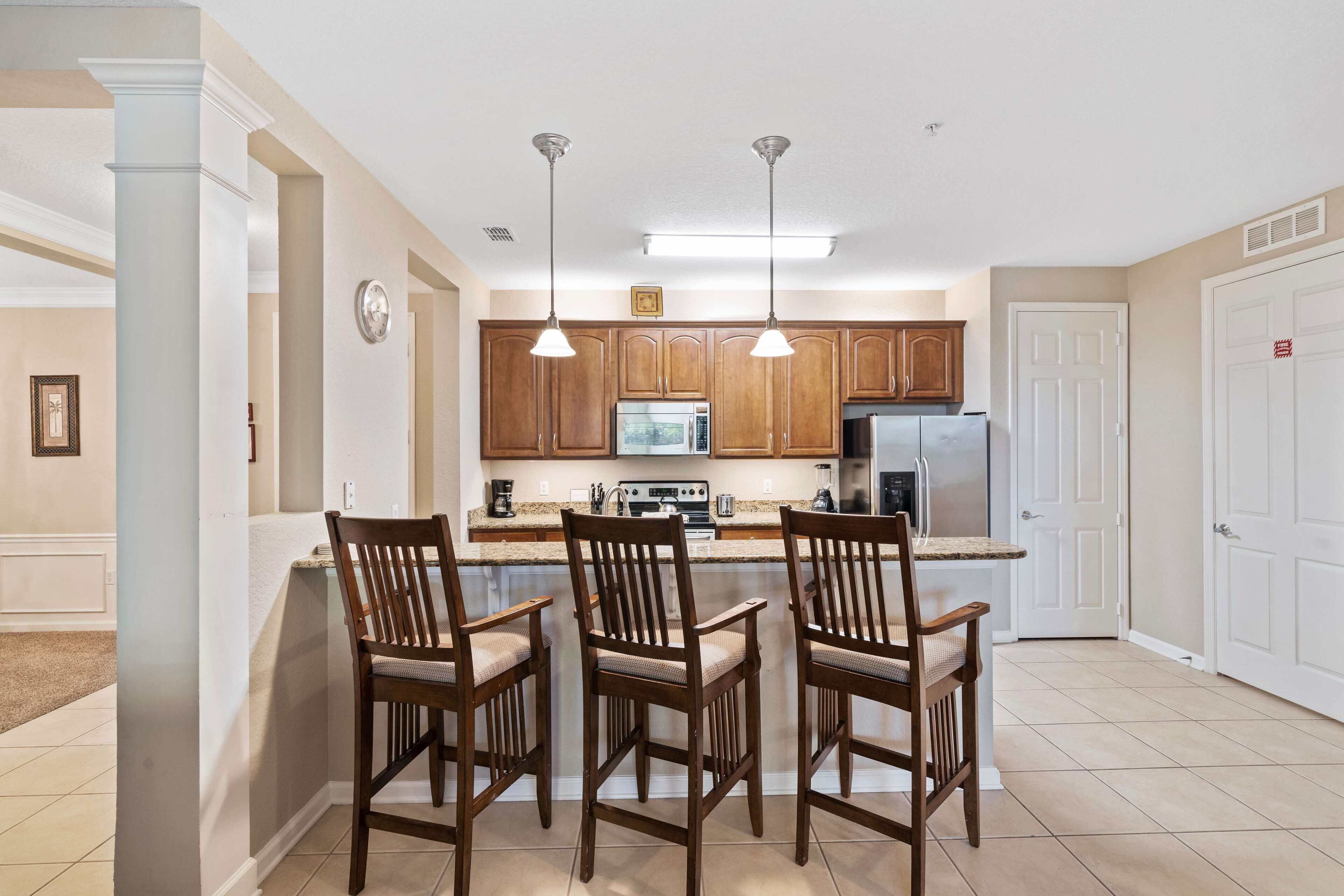 A kitchen with wooden cabinets, a central island with chairs, and a refrigerator.