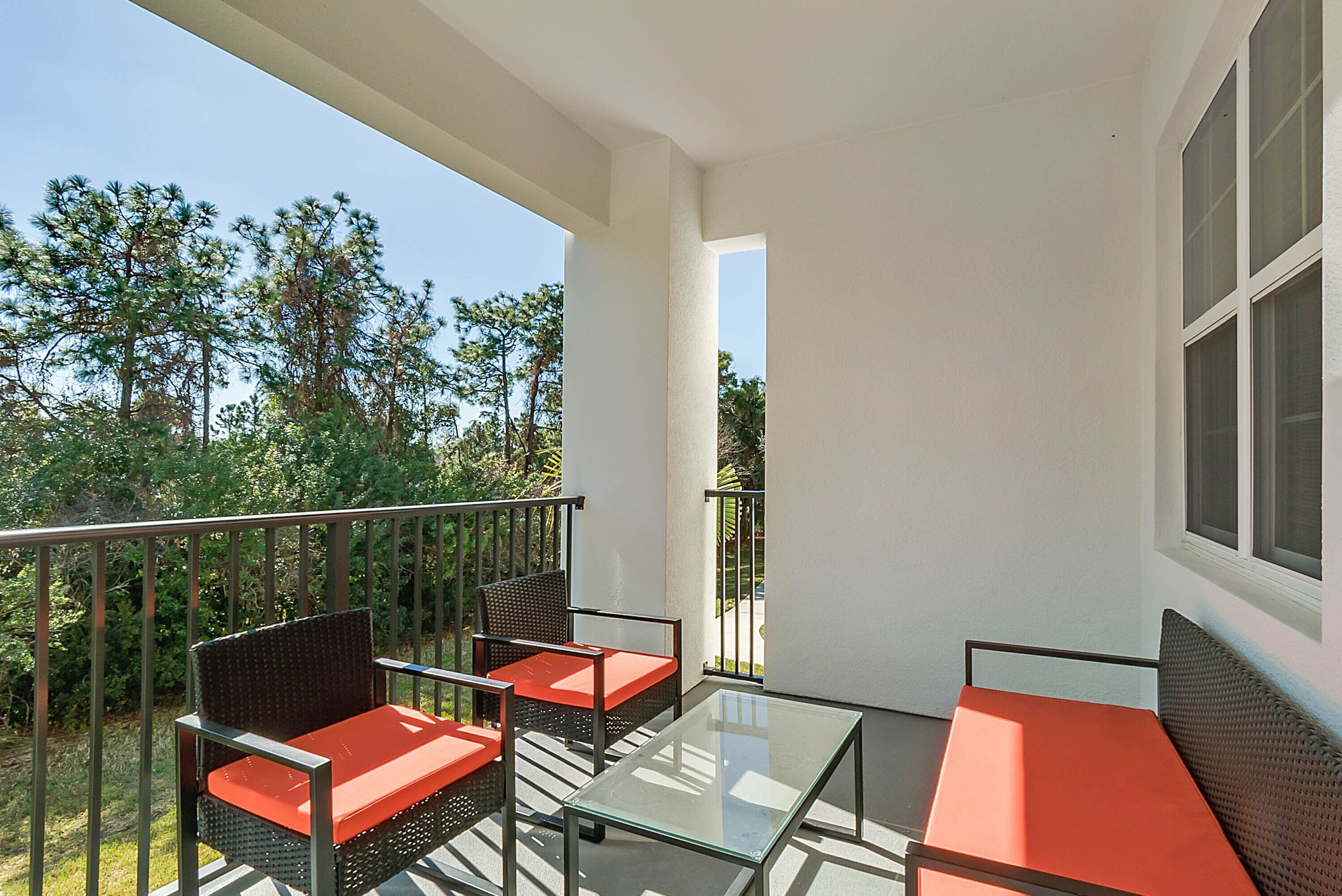 Un balcon agrémenté de meubles en osier et de tables en verre, donnant sur un jardin et des arbres.