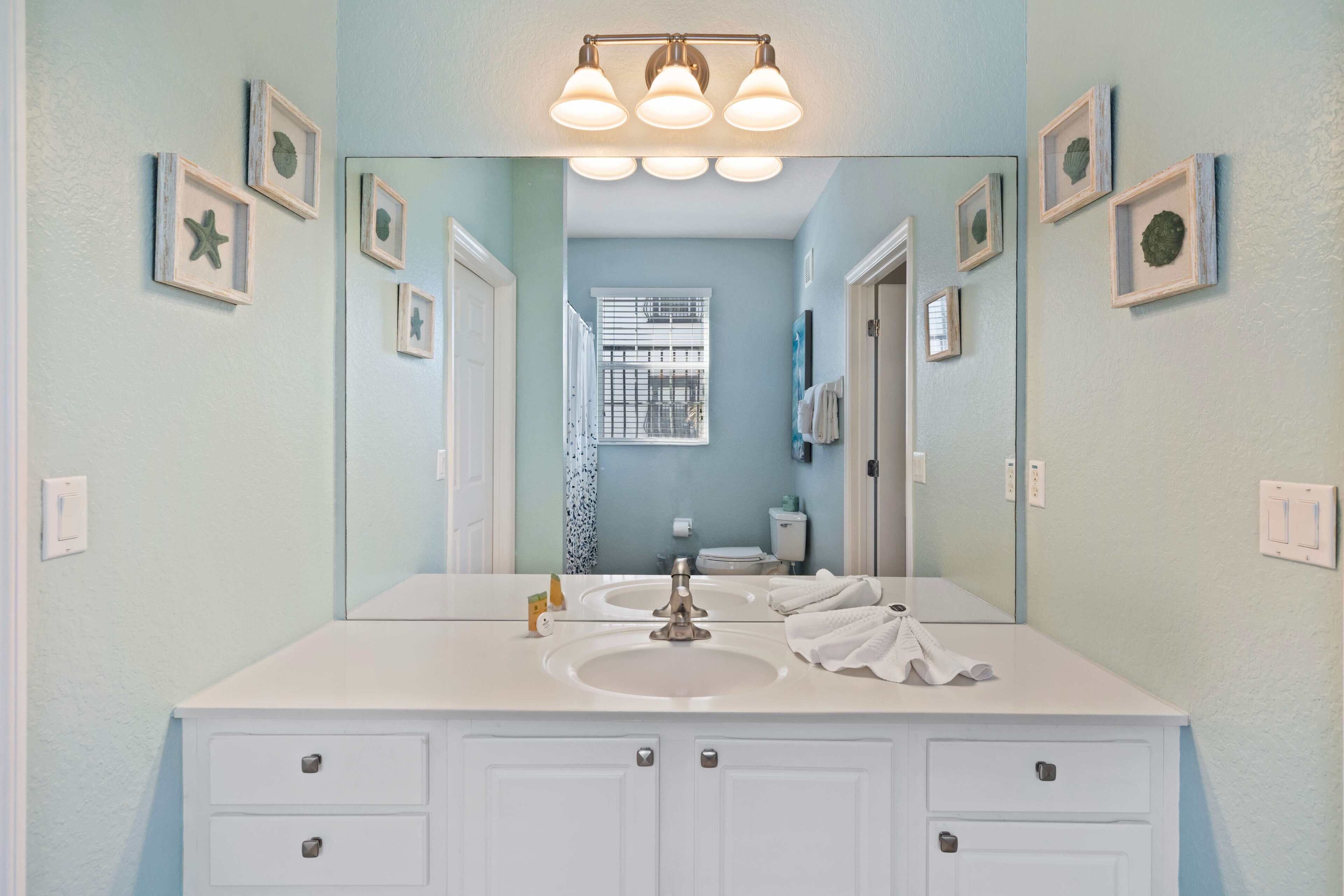 A bathroom with a white vanity, a large mirror, and framed pictures on the walls.