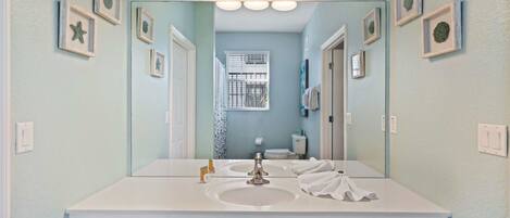 A bathroom with a white vanity, a large mirror, and framed pictures on the walls.