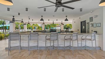 A bar area with a ceiling fan, multiple hanging lights, and a view of the outdoor area with palm trees and umbrellas.