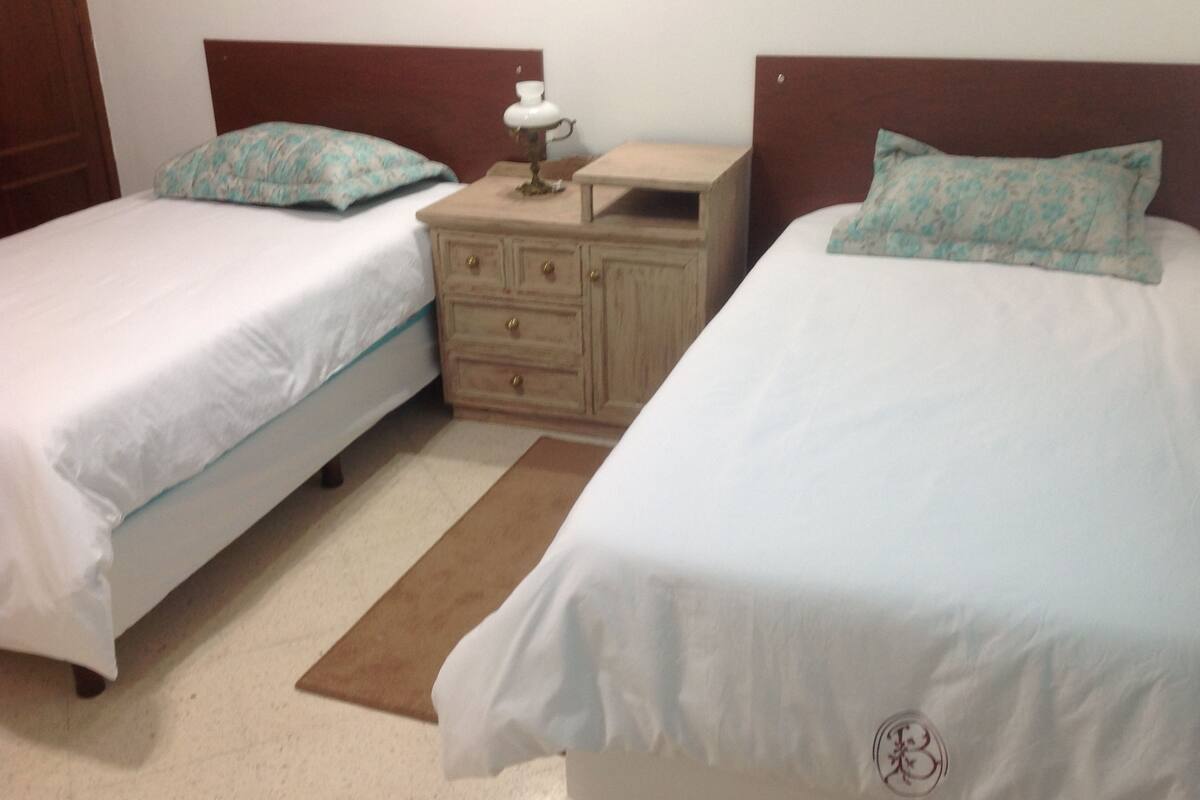A double room with two single beds, a nightstand with a lamp, and a wooden dresser.