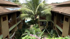 A hotel with a central courtyard featuring a palm tree, surrounded by lush greenery and multiple-story buildings with tiled roofs and balconies. - Pousada Abaré (Itacaré)