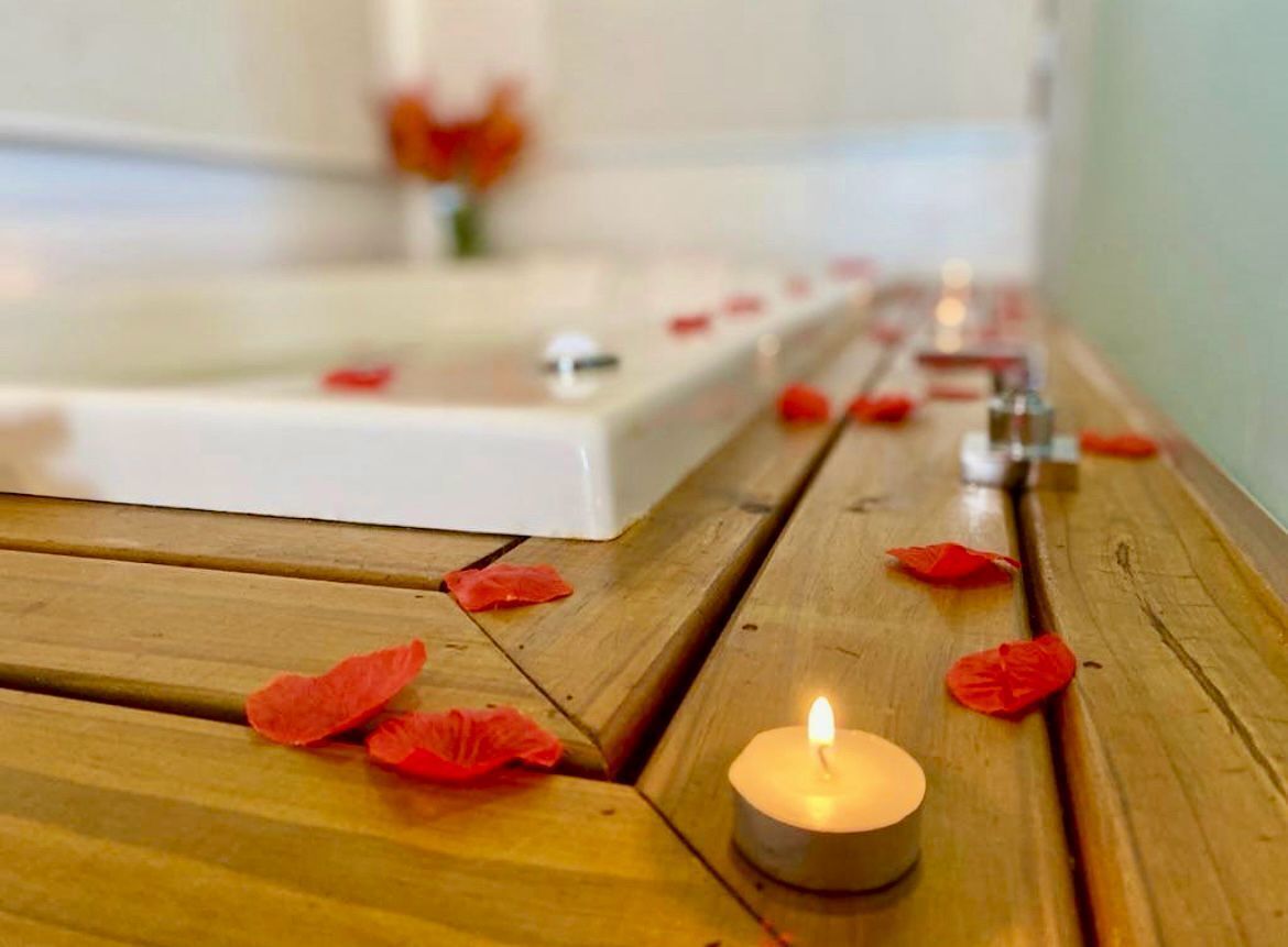 A wooden bench with a lit candle and scattered rose petals.